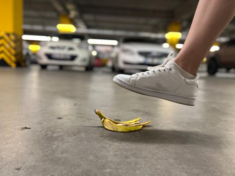 White sneaker hovering above a banana peel on a smooth, gray floor in a parking garage.